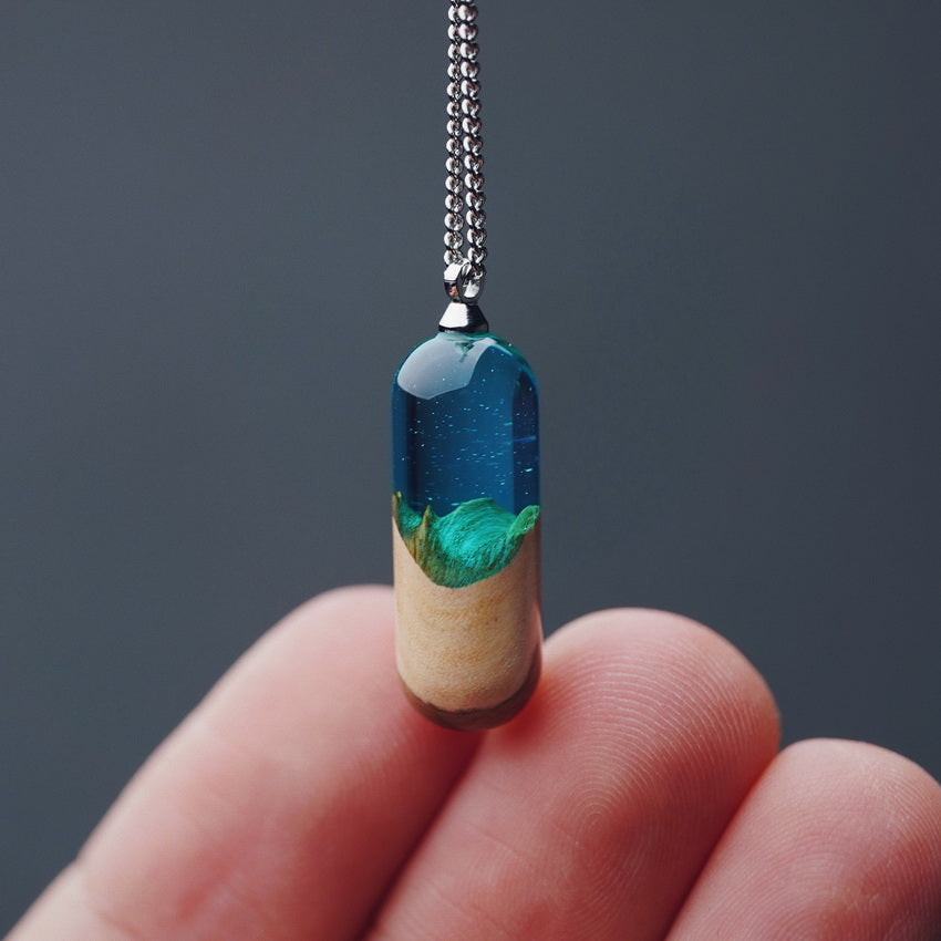 Pendant with a scenic design held between fingers against a dark background