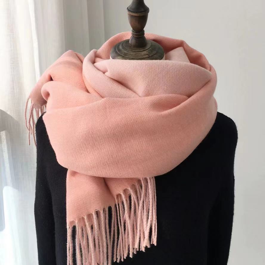 Pink scarf with tassels draped over a black garment on a white background