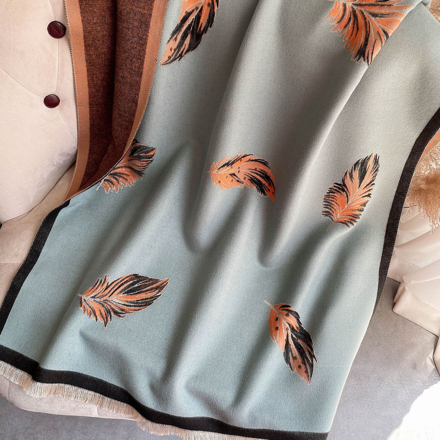 Light blue fabric with orange feather patterns draped over a neutral-colored garment.