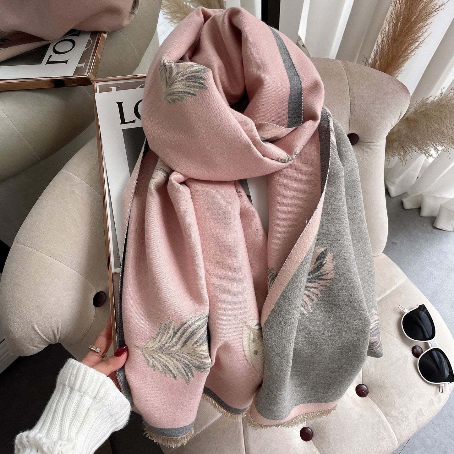 Pink and gray scarf with leaf patterns held by a hand, with a blurred indoor background.