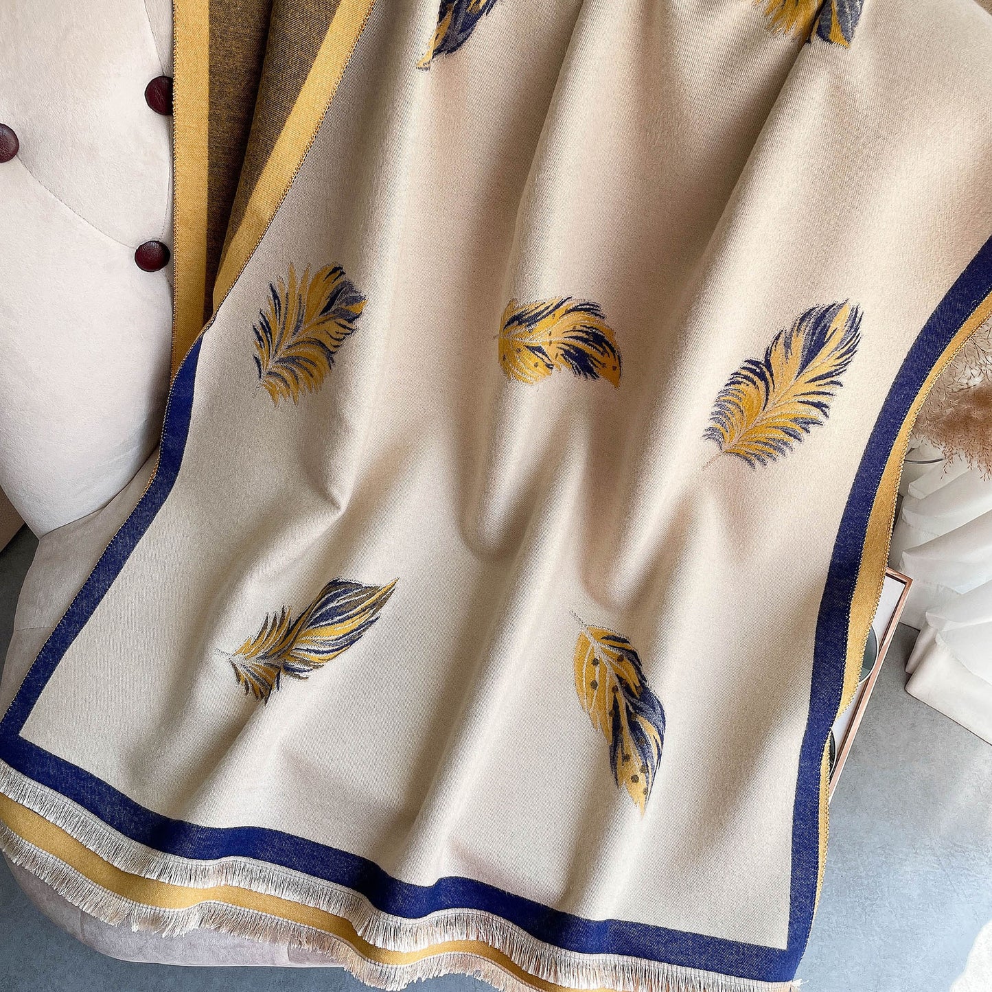 Beige fabric with feather patterns and blue and gold borders on a textured surface.