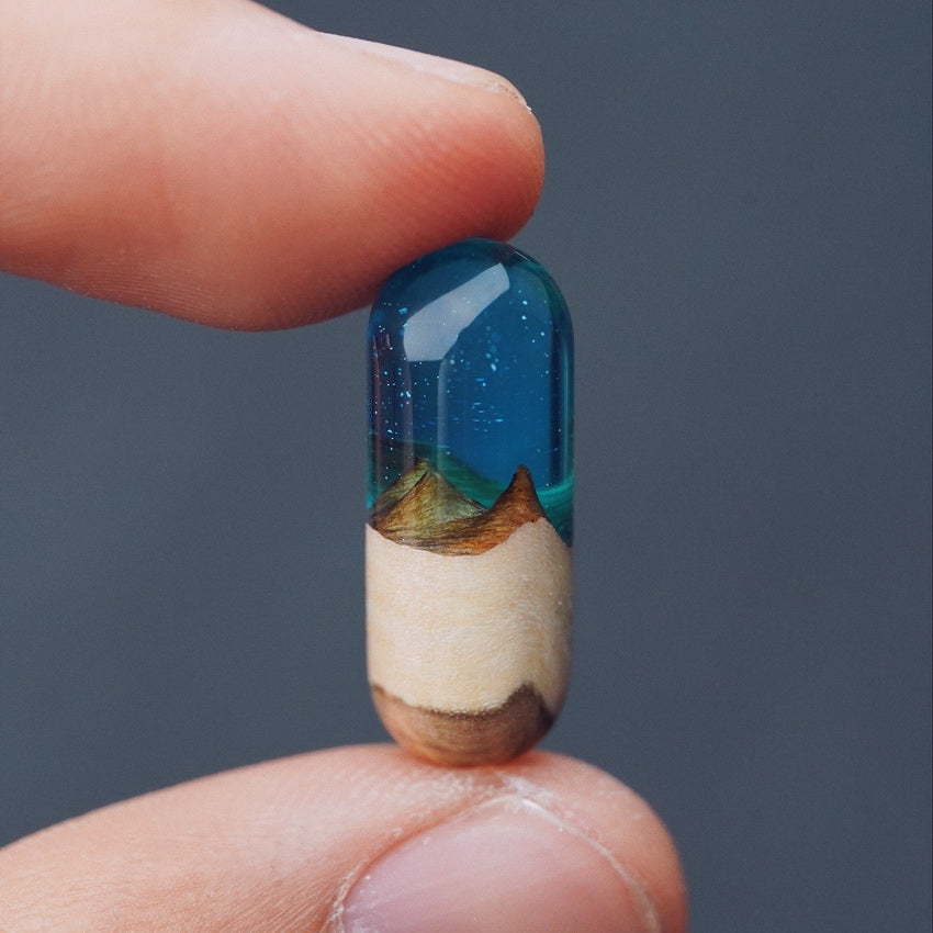 Glass capsule with a scenic design held between fingers against a dark background
